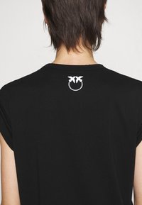 Zwart T-shirt met korte mouwen en een ronde hals, met een wit geborduurd logo van twee vogels in een cirkel op de achterkant.
