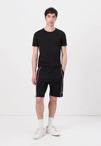 Čierne tričko s krátkymi rukávmi v kombinácii s čiernymi šortkami s bielymi postrannými pruhmi. Model má na sebe biele tenisky a členkové ponožky.