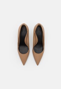 Un paio di scarpe da donna in pelle beige con punta affusolata e solette nere, viste dall'alto su uno sfondo bianco.