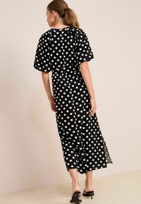 Rochie neagră cu buline albe, cu mâneci scurte tip puff, talie strânsă, lungime medie, slituri laterale, material neted și decolteu rotund.