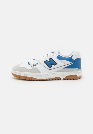Weiß-blauer New Balance 550 Sneaker mit grauen Wildlederakzenten und Gummisohle, von der Seite auf einfarbigem Hintergrund gezeigt.