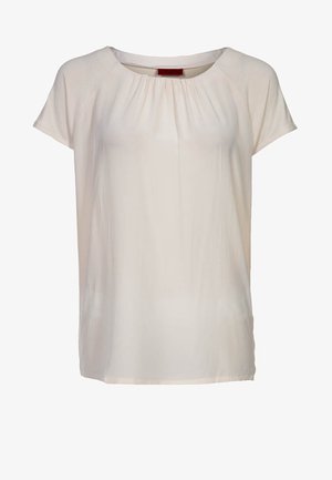 Světlobéžová halenka s krátkými rukávy z hladké látky, má kulatý výstřih se sebráním vpředu a volný střih.