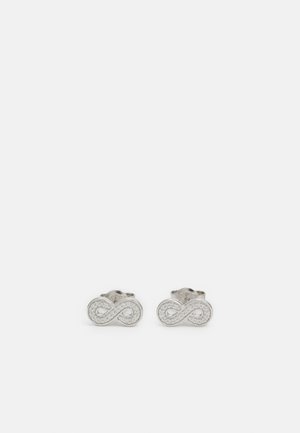 Paire de boucles d'oreilles clous en argent en forme de symbole infini avec de petites pierres incrustées sur fond blanc.