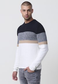 Suéter de punto con rayas horizontales en azul marino, gris, beige y blanco. Textura acanalada con cuello redondo y mangas largas.