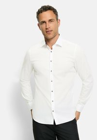 Weißes Langarmhemd mit Button-Down-Kragen und braunen Knöpfen. Verfügt über eine glatte Textur und eine figurbetonte Passform. Trägt dazu eine schwarze Hose.