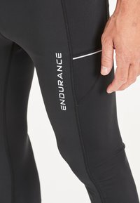 Svarta träningsbyxor med en figurnära design, med en vit logotyp "ENDURANCE" och en sidoficka med en reflexstrimmel.