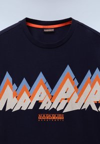 Tricou din bumbac bleumarin cu un grafic viu colorat de munte. Textul include "NAPAPIJRI" în alb și portocaliu cu un model texturat.