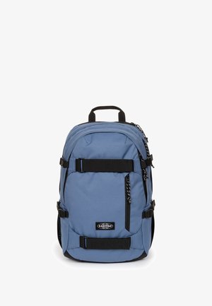 Blå Eastpak rygsæk med sorte stropper, lynlåslommer og et øverste bærehåndtag på en hvid baggrund.