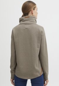 Pullover con colletto in marrone chiaro con pois blu, dotato di un'etichetta sul collo, spacchi laterali e un tessuto morbido e testurizzato.