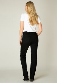 Zwarte denim broek met een aangesloten ontwerp en achterzakken, gecombineerd met een eenvoudig wit t-shirt. Beeld vanuit de achterkant.