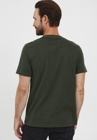 Grønn, kortermet t-skjorte laget av bomull. Har en rund hals og sømdetaljer nær kragen. Glatt tekstur, enkelt design.