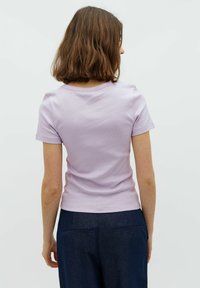 Ibolya színű, rövid ujjú felső bordás textúrával, kerek nyakkivágással és testhezálló kialakítással; sötétkék nadrággal párosítva, amelyek hátul zsebekkel rendelkeznek.