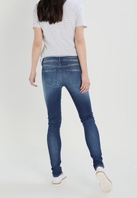 Jeans de denim azul ajustados con un lavado desgastado, que cuentan con bolsillos traseros y un diseño ceñido, combinados con una camiseta a rayas gris y blanca.