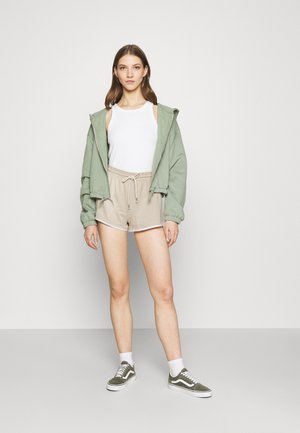 Sweatshirt verde com capuz, t-shirt branca, calções bege com cordão e sapatilhas verdes Vans. Tecido suave, corte descontraído, estilo casual.