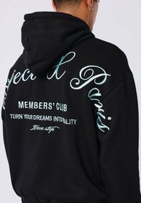 Haut à capuche noir avec du texte en aqua sur le devant et le dos, affichant en gros "Project Paris" et "Members’ Club". Tissu doux et texturé.