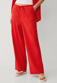 Pantaloni rossi a gamba larga con vita elastica e dettaglio a nodo, realizzati in un tessuto leggero, caratterizzati da una texture liscia e una vestibilità comoda.