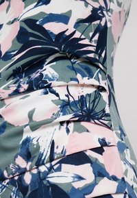 Gros plan sur un tissu à motif floral bleu, vert et rose mettant en valeur des détails textiles superposés et pliés.