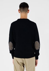 Maglione nero con scollatura rotonda e tessuto testurizzato, con toppe a gomito a quadri in blu navy e beige. Polsini e orlo a costine.