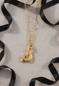 Guldvedhæng i form af en musiknote, hængende på en guldkæde. Omgivet af sorte satinbånd på en struktureret lys overflade.