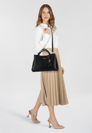 Zwarte leren handtas met een gestructureerd oppervlak, dubbele bovenhandvatten, een afneembare schouderband en een kleine kwastaccent. Het model draagt een witte blouse en een beige plissé rok.