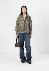 Grønt blomstermønster knappeskjorte med lange ermer, parret med løse blåjeans og en liten mørk håndveske. Glatt stofftekstur.