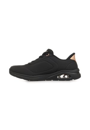 Zwarte atletische sneaker met geperforeerd zijpaneel, veters aan de voorkant, zichtbare luchtkussentjes in de zool en metalen roségouden hieldetail.