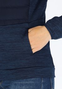 Marineblauwe pullover met een textuurpatroon, voorzien van een zijzak en strakke boorden. Zachte stof met een licht glanzende afwerking.
