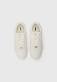 White sneakers with smooth upper, perforated texture on the toe, lace closure, and subtle branding on the tongue and side. Flat sole.