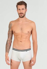 Fehér bokszernadrág fekete csíkkal ellátott derékgumival, puha anyagból készült, szoros illeszkedésű és sima felületű.