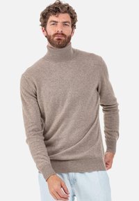 Pull beige à col roulé en tissu doux, avec des manches longues et une coupe ajustée, associé à un jean en denim bleu clair.