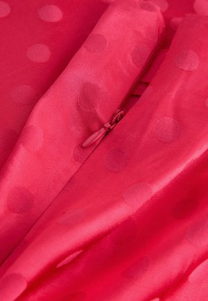 Spilgti rozā audums ar gludu tekstūru, ar paceltām punktiņiem. Vienā malā ir redzams slēpts rāvējslēdzējs.