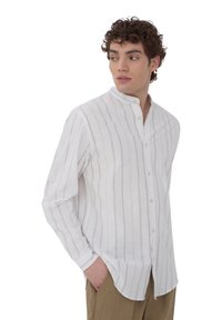 Camicia di lino bianca con righe verticali marrone chiaro, colletto alla coreana con bottoni, maniche lunghe e vestibilità rilassata. Texture morbida, stile casual.