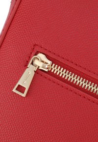 Pouch in pelle rossa con finitura testurizzata, dotata di una cerniera in tono oro e un tirante, che presenta dettagli di cucitura intricati.