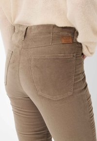Braune Corduroyhose mit glatter Textur, Fünf-Taschen-Design und einem Lederlabel am hinteren Bund. Slim Fit mit genähten Details.