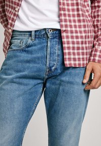 Light blue denim jeans with a straight-leg design, five pockets, and a button closure, paired with a red and white checked shirt.