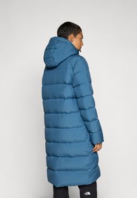 Blue puffer coat with a hood, featuring a quilted design and long silhouette. Made from smooth, water-resistant fabric, with elastic cuffs.