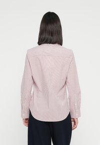 Chemise à manches longues à rayures rouges et blanches, avec un ourlet incurvé, des poignets boutonnés et un détail au dos. Fabriquée en tissu léger.