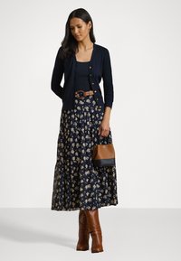 Cardigan navy con chiusura a bottoni, top nero, gonna floreale navy, cintura marrone, stivali marroni e una piccola borsa marrone e nera.
