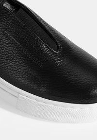 Schwarze Leder-Slipper-Sneaker mit elastischen Seitenpanelen, einer strukturierten Oberfläche und einer weißen Gummisohle mit einem strukturierten Griff.