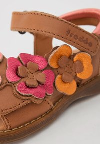 Bruna lädersandaler med blommiga accenter i rosa, orange och ljusbrun. Har en krok-och-slinga rem och en texturerad yta.