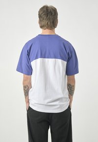 Short-sleeve t-shirt featuring a divided color design: purple upper half and white lower half, made from soft cotton, with a relaxed fit.