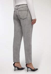 Jeans in denim grigio a vita alta con una vestibilità dritta, design a cinque tasche, cuciture visibili e caviglie svasate, indossati con scarpe col tacco nere.