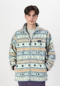 Veste en polaire zippée avec un motif comportant des bleus, des oranges et des crèmes ; comprend un col montant et deux poches latérales.