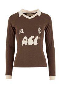 Ruskea pitkähihaine paita, jossa on valkoinen kaulus ja hihansuut. Paidassa on suuri valkoinen logo ja pieni emblem rintakehässä. Pehmeää puuvillamateriaalia.