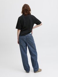 Črna oversize majica, kratki rokavi, gladka tekstura; ohlapni modri jeans z zadnjimi žepi; svetlo rjavi čevlji.