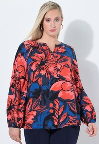 Blusa floreale con sfondo blu navy, caratterizzata da grandi fiori rossi e blu. Scollo semplice, maniche lunghe e vestibilità ampia.