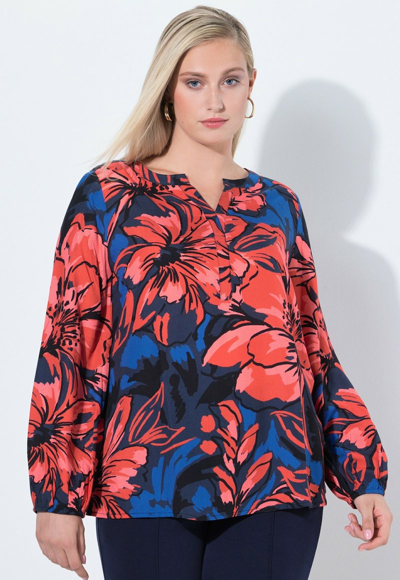 Blusa floreale con sfondo blu navy, caratterizzata da grandi fiori rossi e blu. Scollo semplice, maniche lunghe e vestibilità ampia.