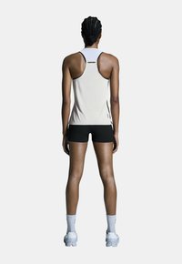 Top corto de tirantes en un color claro con textura, combinado con pantalones cortos negros. El conjunto presenta detalles en contraste y zapatillas de running blancas.