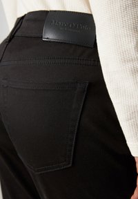 Pantaloni neri con finitura testurizzata, caratterizzati da una tasca posteriore e un'etichetta in pelle con il logo "Marc O'Polo" impresso in vita.