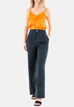 Top in satin arancione con pizzo e pantaloni a vita alta blu navy con bottoni frontali e gamba larga. Il modello indossa sandali neri.